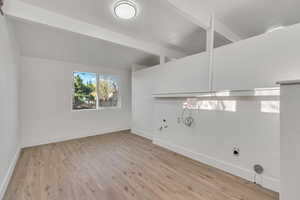 Laundry area featuring light wood-style floors and vaulted ceiling with beams