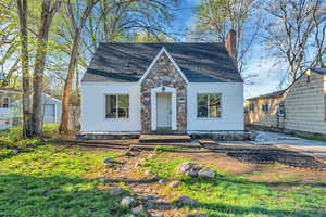 View of front of house featuring a chimney, a shingled roof, stone siding, and a front lawn