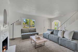 Carpeted living area featuring healthy amount of natural light, a lit fireplace, and arched walkways