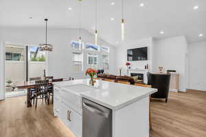 Kitchen with dishwasher, white cabinets, light stone countertops, hanging light fixtures, and vaulted ceiling