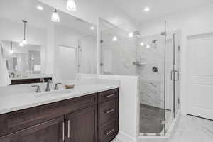 Bathroom with a marble finish shower, vanity, light marble finish flooring, and recessed lighting