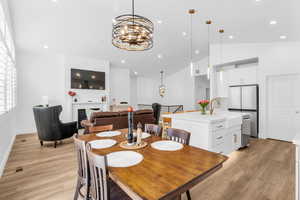 Dining area with a chandelier, light wood-style floors, a fireplace, and lofted ceiling