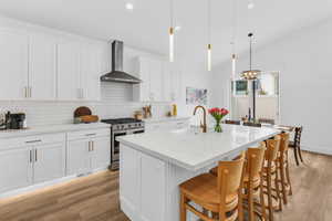 Kitchen with gas range, white cabinets, light wood-style floors, a kitchen breakfast bar, and a center island with sink