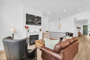 Living room with light wood finished floors, vaulted ceiling, a glass covered fireplace, and suspended lighting