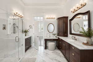 Bathroom with two vanities, a marble finish shower, ornamental molding, and light marble finish floors