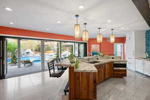 Kitchen with dual tone cabinets, light tile patterned floors, hanging light fixtures, an island with sink, and stainless steel microwave