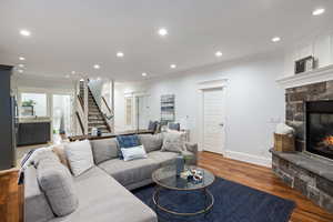 Living room featuring a stone fireplace, wood finished floors, recessed lighting, and ornamental molding