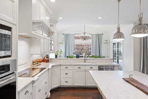 Kitchen with stainless steel appliances, white cabinetry, glass insert cabinets, dark wood-type flooring, and vaulted ceiling