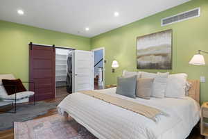 Bedroom with a barn door, a spacious closet, stacked washer and clothes dryer, wood finished floors, and recessed lighting