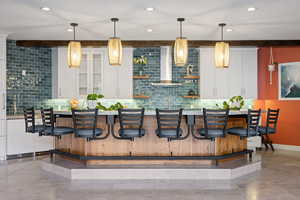Kitchen with white cabinets, a breakfast bar, tasteful backsplash, and beamed ceiling