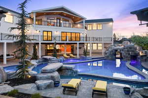 Back of property at dusk featuring a balcony, a patio area, and a pool with connected hot tub