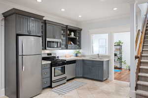 Kitchen with stainless steel appliances, gray cabinetry, light tile patterned floors, glass insert cabinets, and recessed lighting