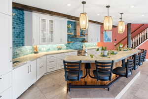 Kitchen with a kitchen breakfast bar, white cabinetry, backsplash, glass fronted cabinets, and a spacious island