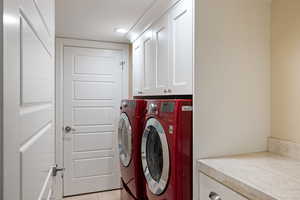 Laundry room with independent washer and dryer, light tile patterned floors, and cabinet space