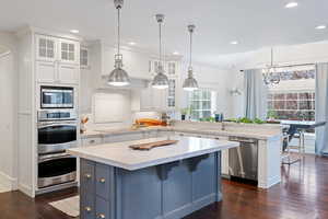 Kitchen with a peninsula, a breakfast bar, glass fronted cabinets, stainless steel appliances, and dual tone cabinets