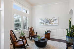 Living area with wood finished floors, ornamental molding, a decorative wall, and a wainscoted wall