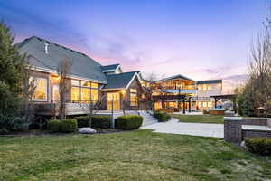 Back of house at dusk featuring a yard, a shingled roof, a patio area, a balcony, and brick siding
