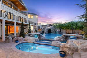 Pool at dusk featuring a patio, a balcony, and a pool with connected hot tub