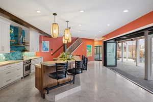 Dual tone kitchen featuring a breakfast bar area, open shelves, hanging light fixtures, two tone cabinets, and stainless steel oven
