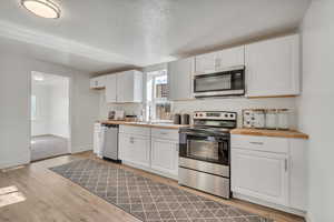 Kitchen with stainless steel appliances, white cabinets, light wood-style floors, butcher block counters, and a textured ceiling