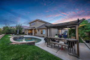 Rear view of house featuring a patio, a pool with connected hot tub, outdoor dining space, a lawn, and stucco siding