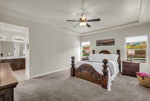 Bedroom with light colored carpet, ceiling fan, a tray ceiling, and ensuite bath