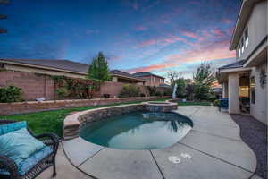 Pool at dusk featuring a patio, a fenced backyard, and a pool with connected hot tub