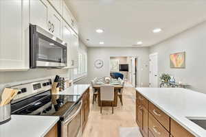 Kitchen with stainless steel appliances, light wood-style flooring, recessed lighting, light stone countertops, and open floor plan