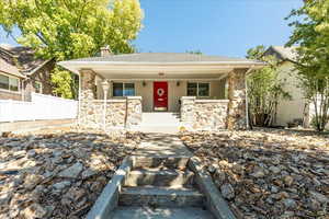 View of front of property featuring covered porch, stone siding, a chimney, a shingled roof, and stucco siding