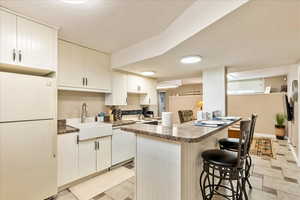 Kitchen with white appliances, dark countertops, a kitchen breakfast bar, and white cabinetry