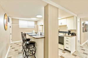 Kitchen with white appliances, a kitchen bar, white cabinetry, and a peninsula
