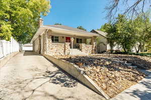 View of front of property with covered porch, a chimney, stone siding, and a shingled roof