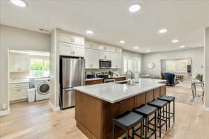Kitchen with dual tone cabinets, stainless steel appliances, light wood-style flooring, a kitchen island with sink, and a kitchen bar