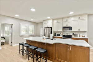 Kitchen featuring stainless steel appliances, two tone cabinets, light wood-style flooring, a center island with sink, and a kitchen bar