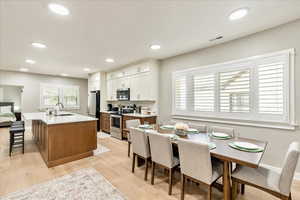 Two tone kitchen with stainless steel appliances, a kitchen island with sink, a kitchen breakfast bar, light wood-style flooring, and two tone color scheme