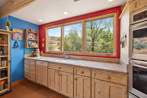 Kitchen with stainless steel double oven, light stone countertops, light wood finish cabinetry, and dark tile patterned floors
