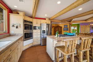 Kitchen featuring recessed lighting, stainless steel appliances, a kitchen bar, beam ceiling, and dark tile patterned flooring