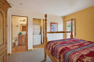 Bedroom with stacked washer and dryer, connected bathroom, and light tile patterned floors