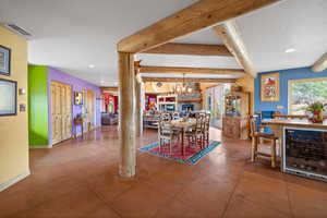 Dining room featuring wine cooler, tile patterned flooring, beam ceiling, a chandelier, and a fireplace