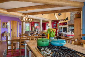 Dining room with suspended lighting, a stone fireplace, beamed ceiling, and beverage cooler