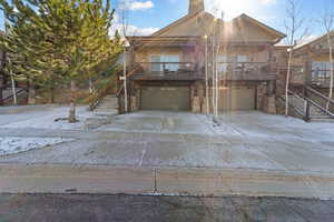 Rustic home with an attached garage, a deck, concrete driveway, and stone siding