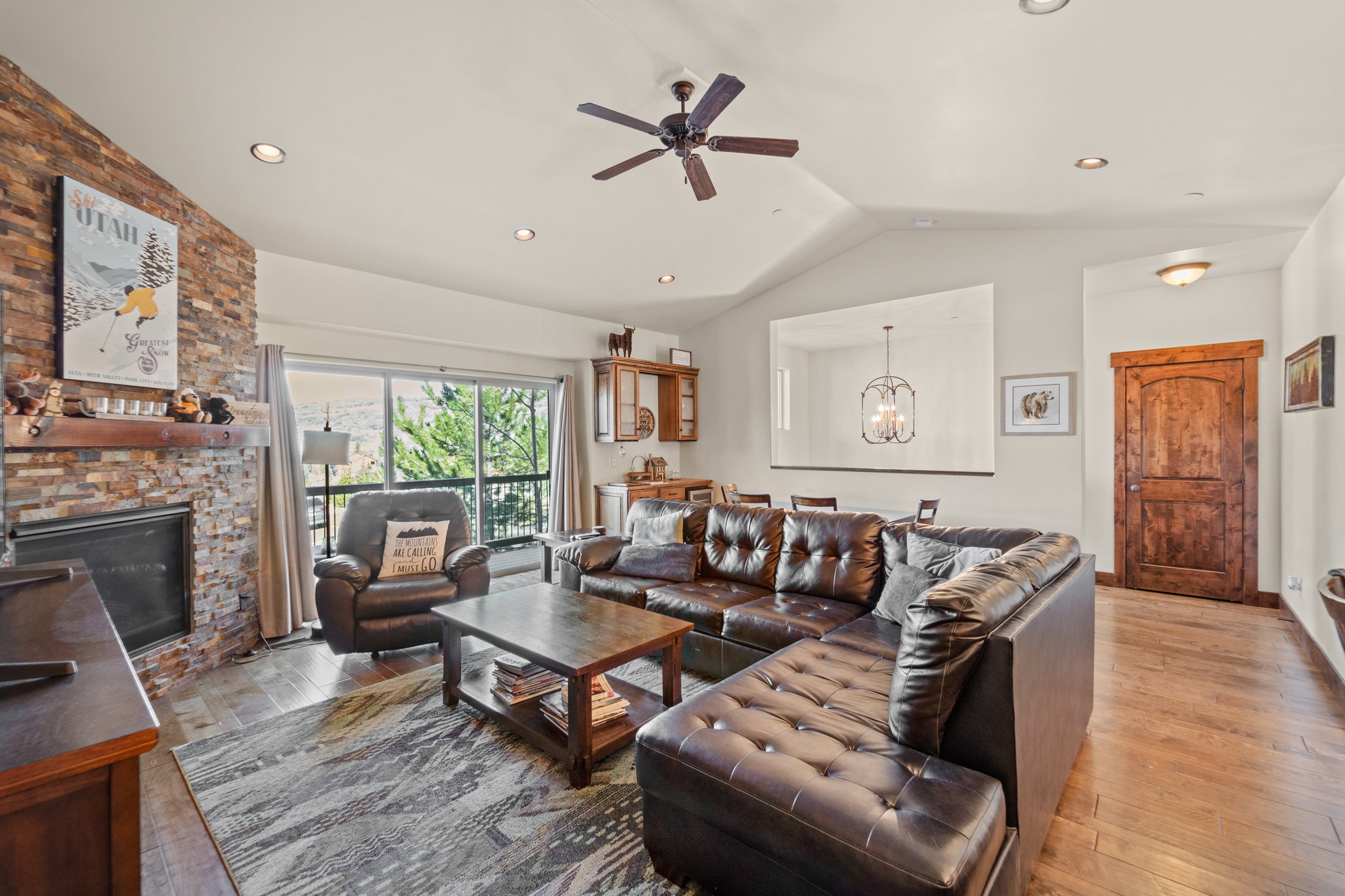 Living area featuring a ceiling fan, light wood finished floors, a chandelier, a stone fireplace, and vaulted ceiling