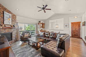 Living area featuring a ceiling fan, light wood finished floors, a chandelier, a stone fireplace, and vaulted ceiling