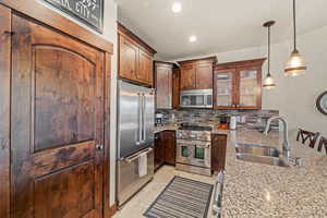 Kitchen featuring high end appliances, light stone countertops, tasteful backsplash, glass fronted cabinets, and a peninsula