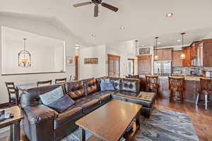 Living room with dark wood-style flooring, ceiling fan, a chandelier, and vaulted ceiling