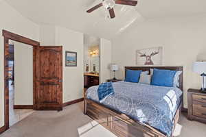 Bedroom featuring vaulted ceiling, light colored carpet, connected bathroom, and a ceiling fan