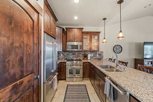 Kitchen featuring high end appliances, light stone countertops, decorative backsplash, a peninsula, and decorative light fixtures