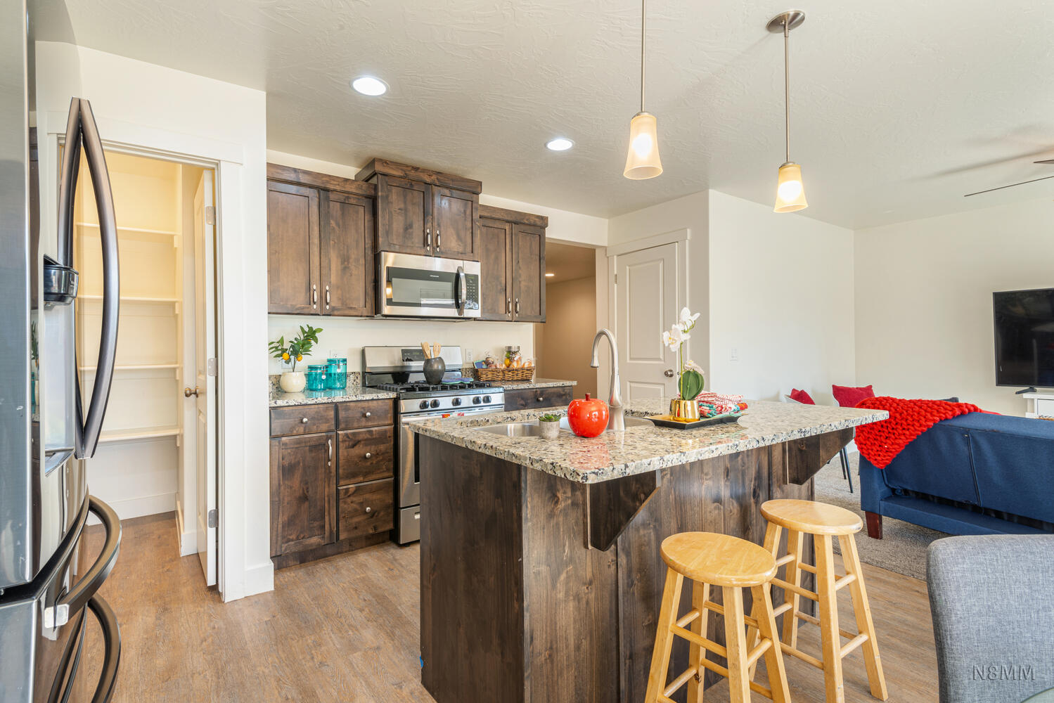 Kitchen with open floor plan, stainless steel appliances, dark wood finish cabinetry, light wood finished floors, and hanging light fixtures