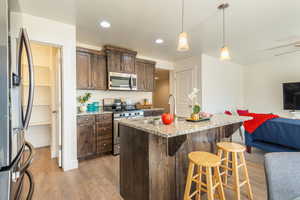 Kitchen with open floor plan, stainless steel appliances, dark wood finish cabinetry, light wood finished floors, and hanging light fixtures