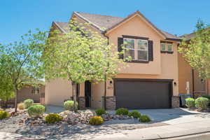 View of front of property with a garage, driveway, stone siding, and stucco siding